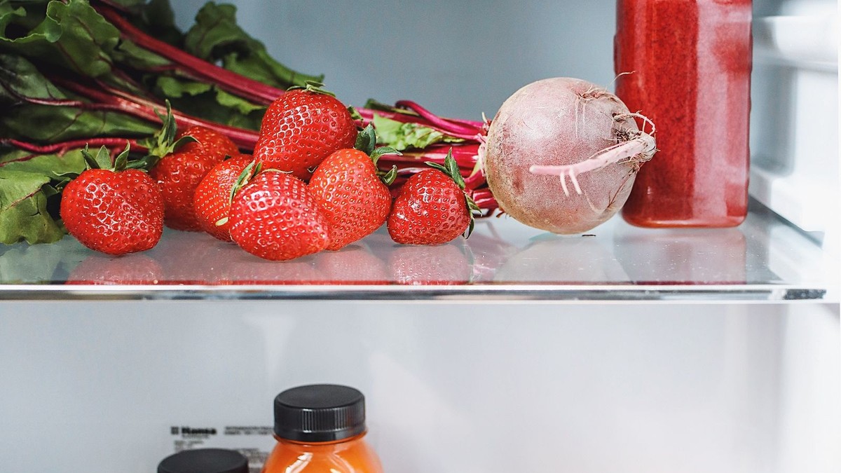 An organized refrigerator with clear stackable bins, a can dispenser, and labeled containers