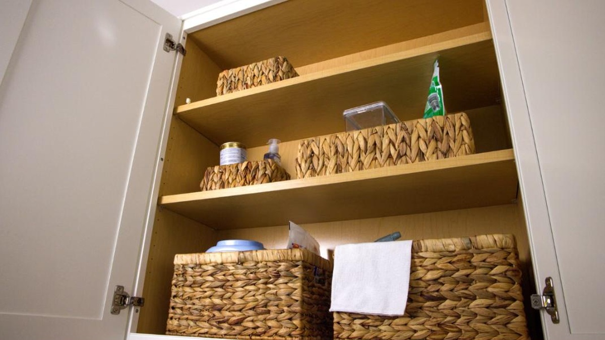 An organized under-sink bathroom cabinet with a two-tier pull-out shelf and labeled bins around the pipes